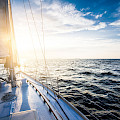 © Alex Stemmers | stock.adobe.com | (White yacht sailing at sunset. A view from the yacht's deck to the bow and sails. Baltic sea, Latvia)