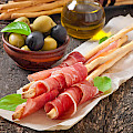 © timolina | freepik.com | (Grissini bread sticks with ham, olives, basil on old wood)